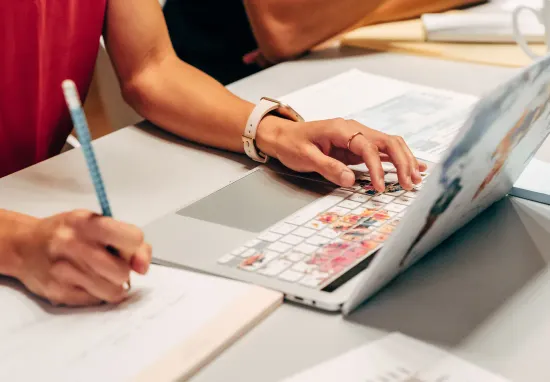 Hands copying a paper list into a spreadsheet on a laptop